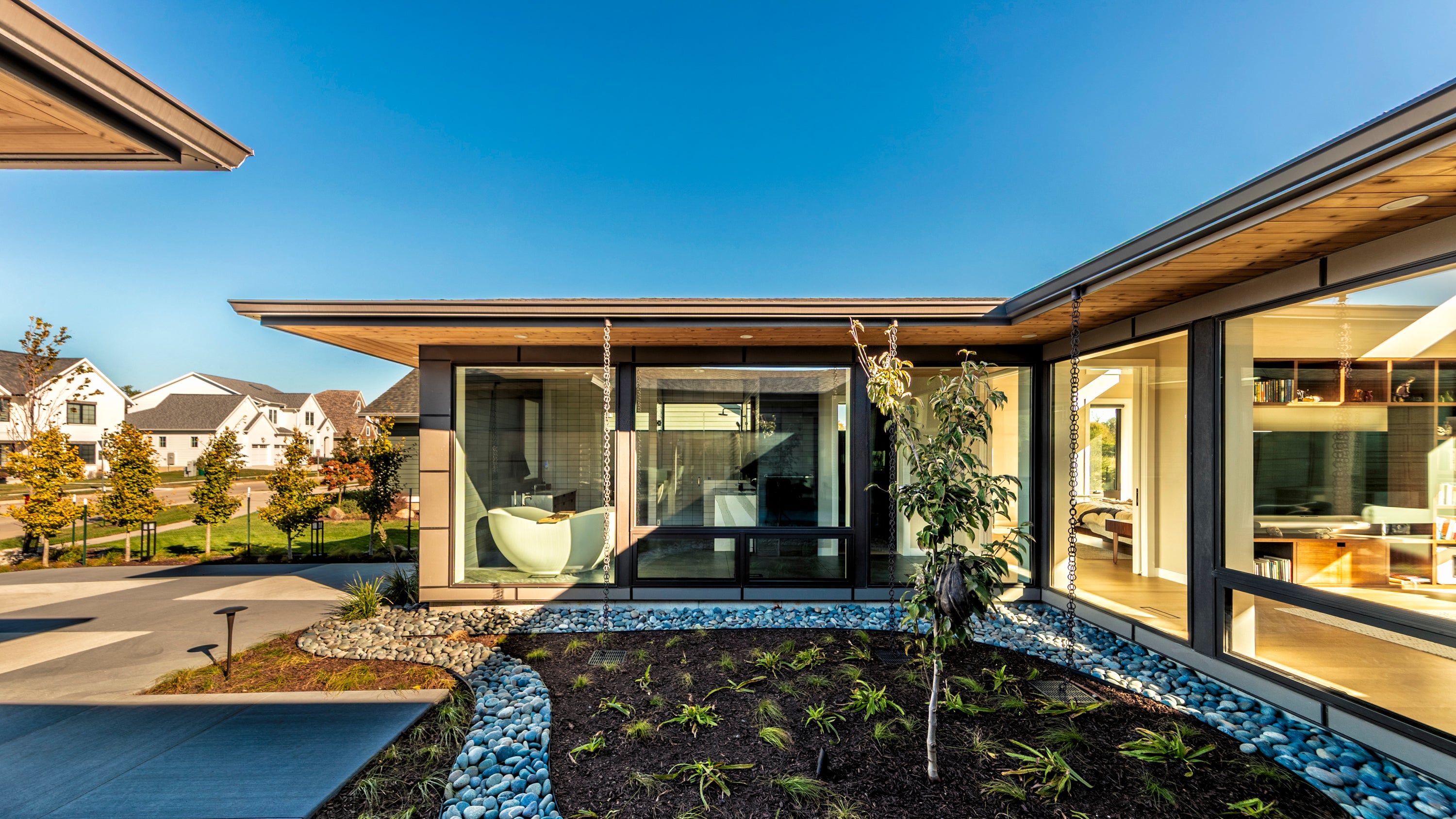 Modern house courtyard with large glass windows and a clear blue sky.